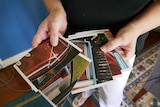 Hands hold a set of photographs that are fanned out and display rust and piping.