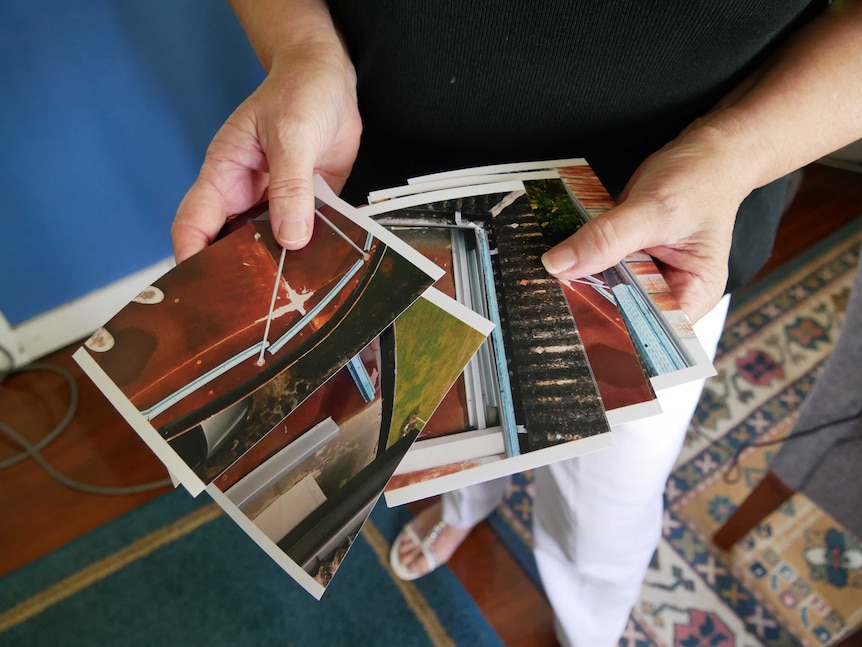 Hands hold a set of photographs that are fanned out and display rust and piping.