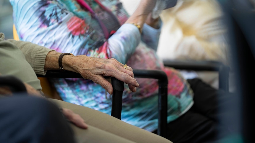 An elderly person's hand rests on a chair.
