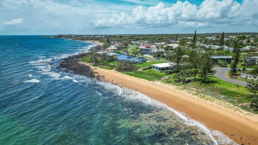 An aerial photo of the ocean and beach in the foreground and houses along the coast