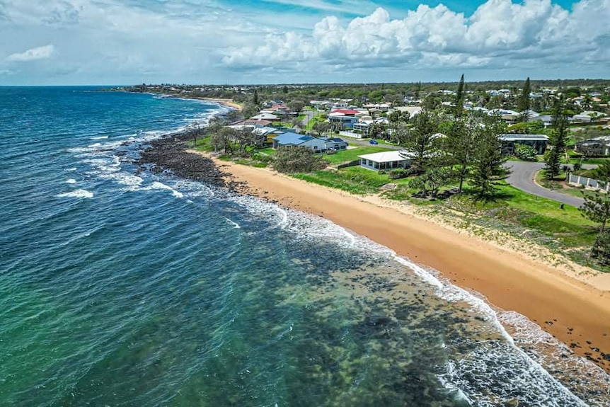 Una fotografía aérea del océano y la playa en primer plano y las casas a lo largo de la costa.