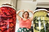 Two jars of fermented fruit and veggies, with a woman doing a thumbs up behind them.