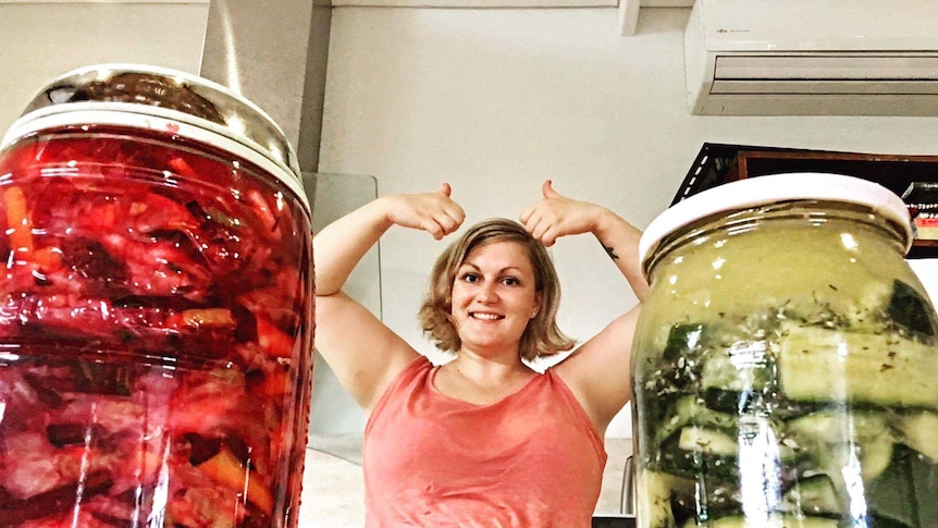 Two jars of fermented fruit and veggies, with a woman doing a thumbs up behind them.