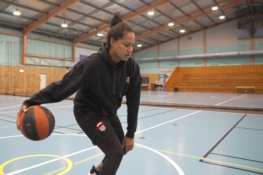 A woman is dribbling by herself on a basketball court.