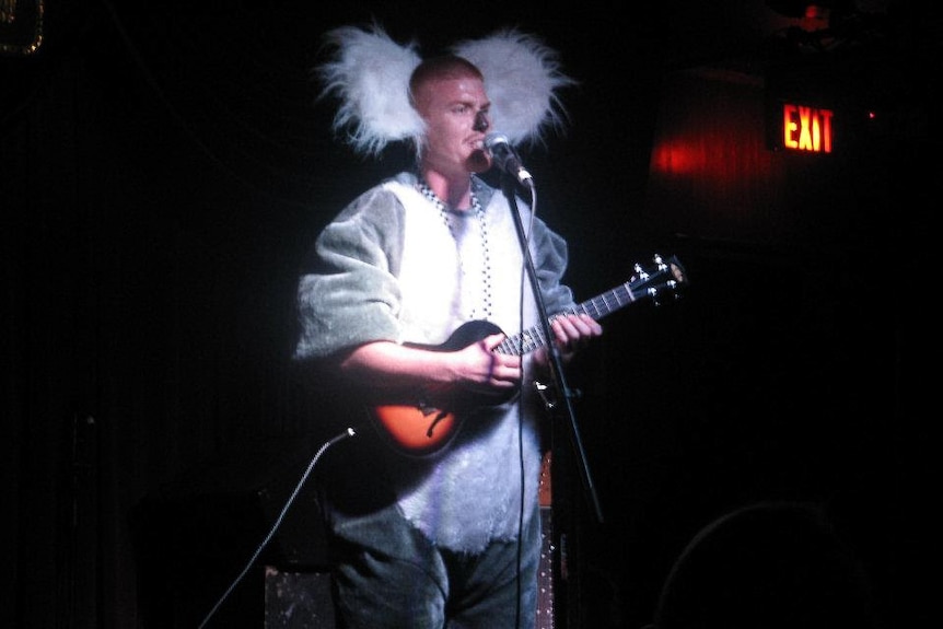 A man dressed in a koala suit playing a guitar and talking into a microphone