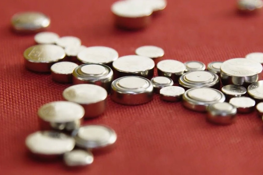 Assorted button batteries sitting on a red carpet.