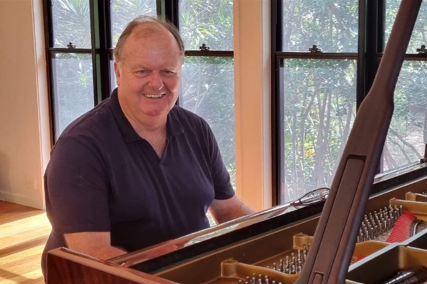 Man in polo shirt smiling at piano