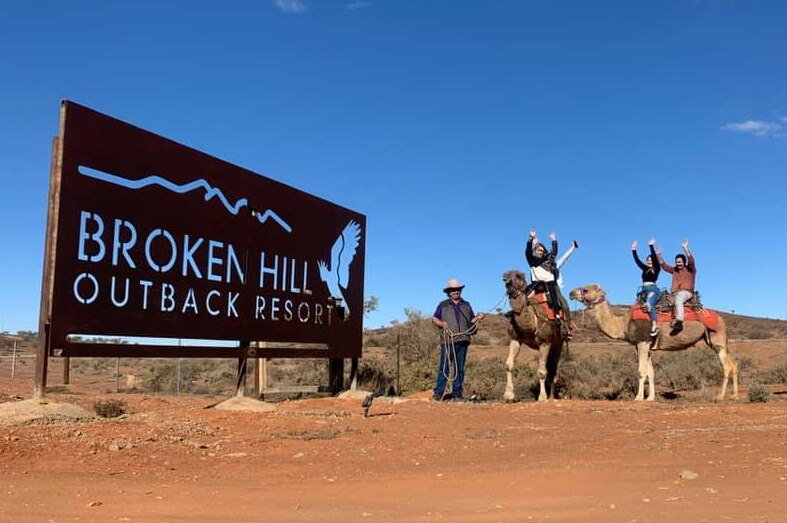 Broken Hill Outback Resort sign post with two camels being ridden by excited riders.