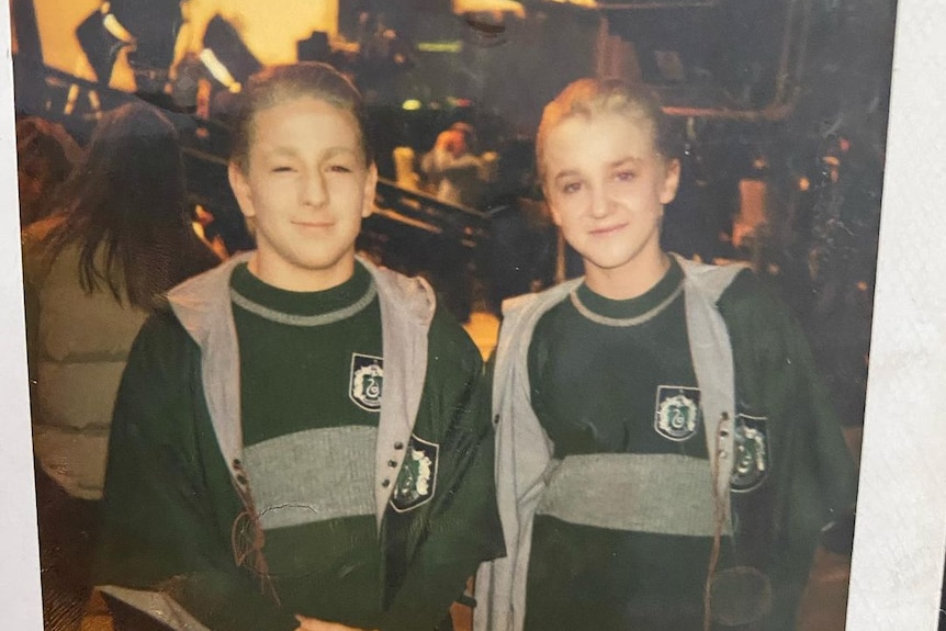 David, dressed as Draco, stands with Tom Felton in identical green Slytherin Quidditch uniforms.