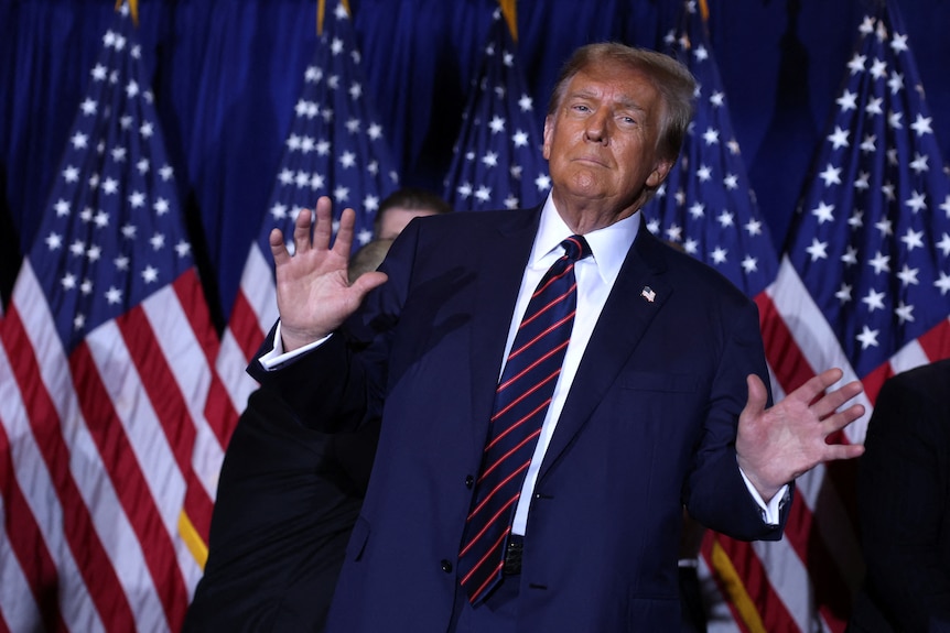 Donald Trump holding up his hands in front of US flags.