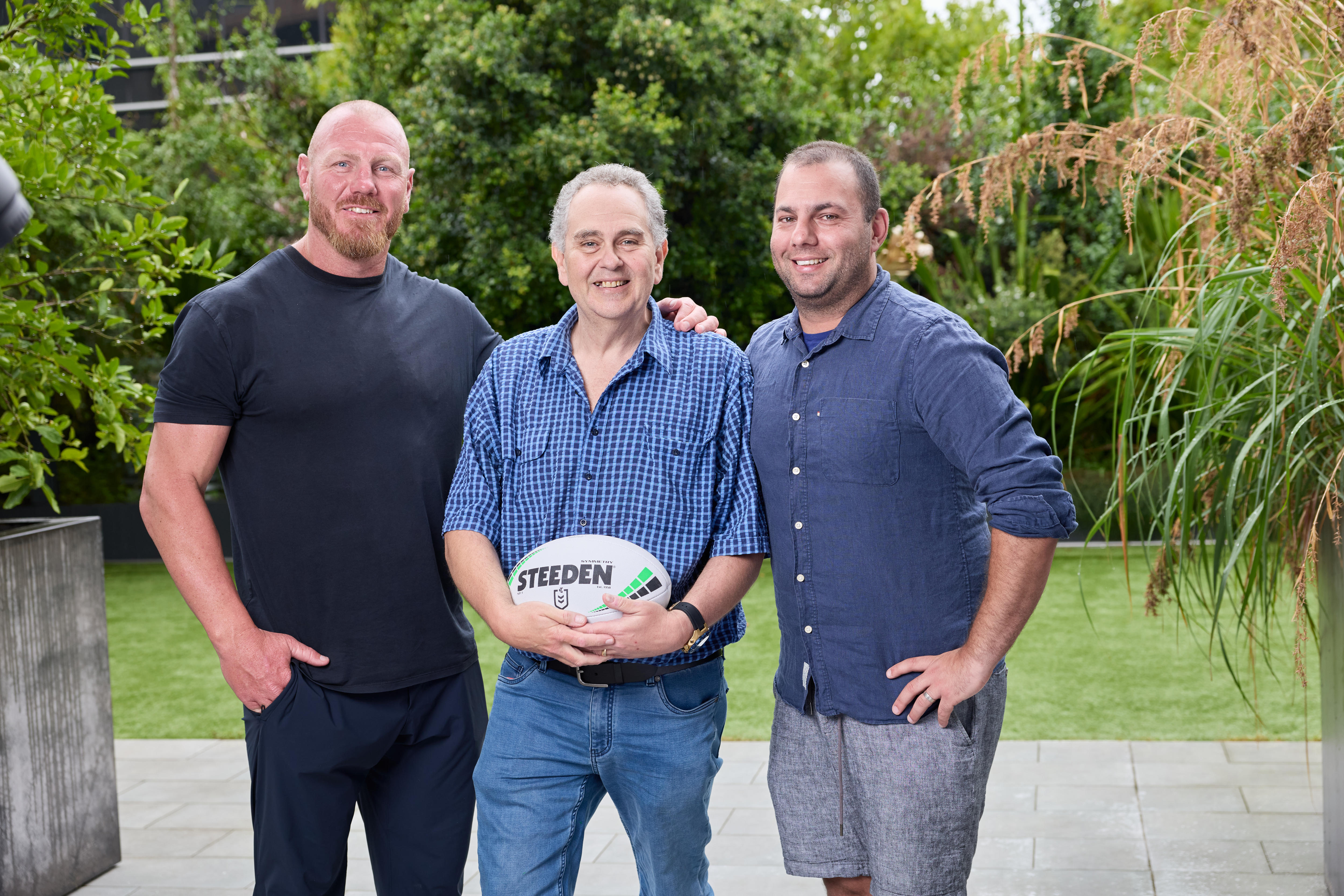 Three men pose together, one holding a football
