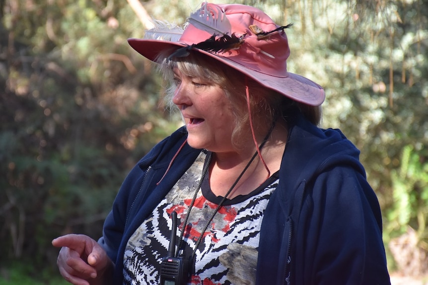 Karen Anderson, dressed in a red hat and blue jacket, stands in the bush addressing her class.