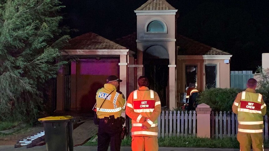 A police officer and two firefighters stand outside a Midvale house at night with the front of the house damaged by fire.