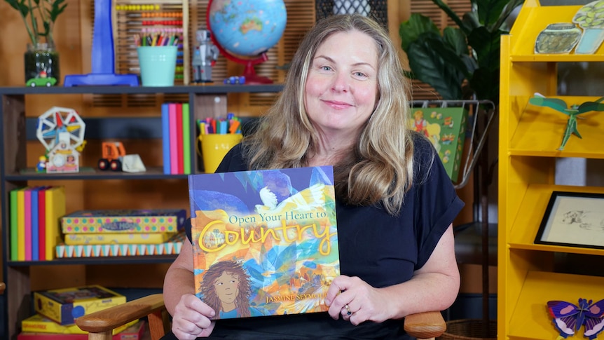 Jasmine Seymour holds up story book with title Open Your Heart to Country