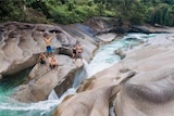 An aerial image of five people standing and crouching on a rock next to fast moving water.