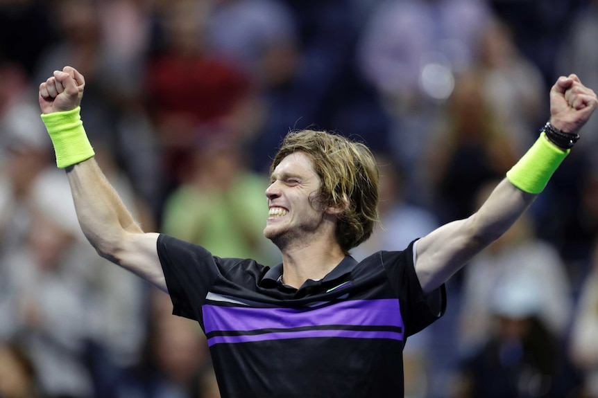 A grinning tennis player raises his arms and closes his eyes in triumph after winning a match.