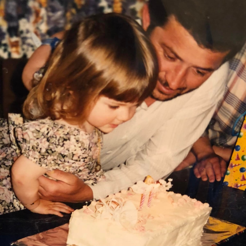 A father and daughter lean over a birthday cake.