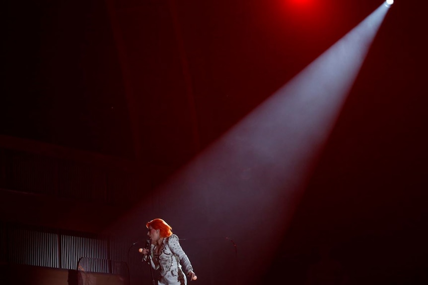 Lady Gaga performs on a bare stage under lights