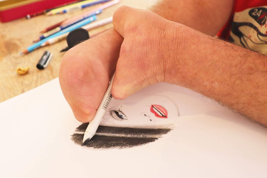 A photo of Robert Drew holding a pencil and sketching a picture