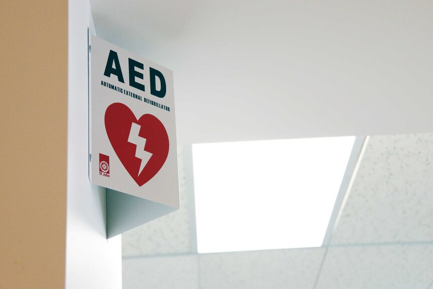 A sign for a defibrillator is mounted on an office wall.