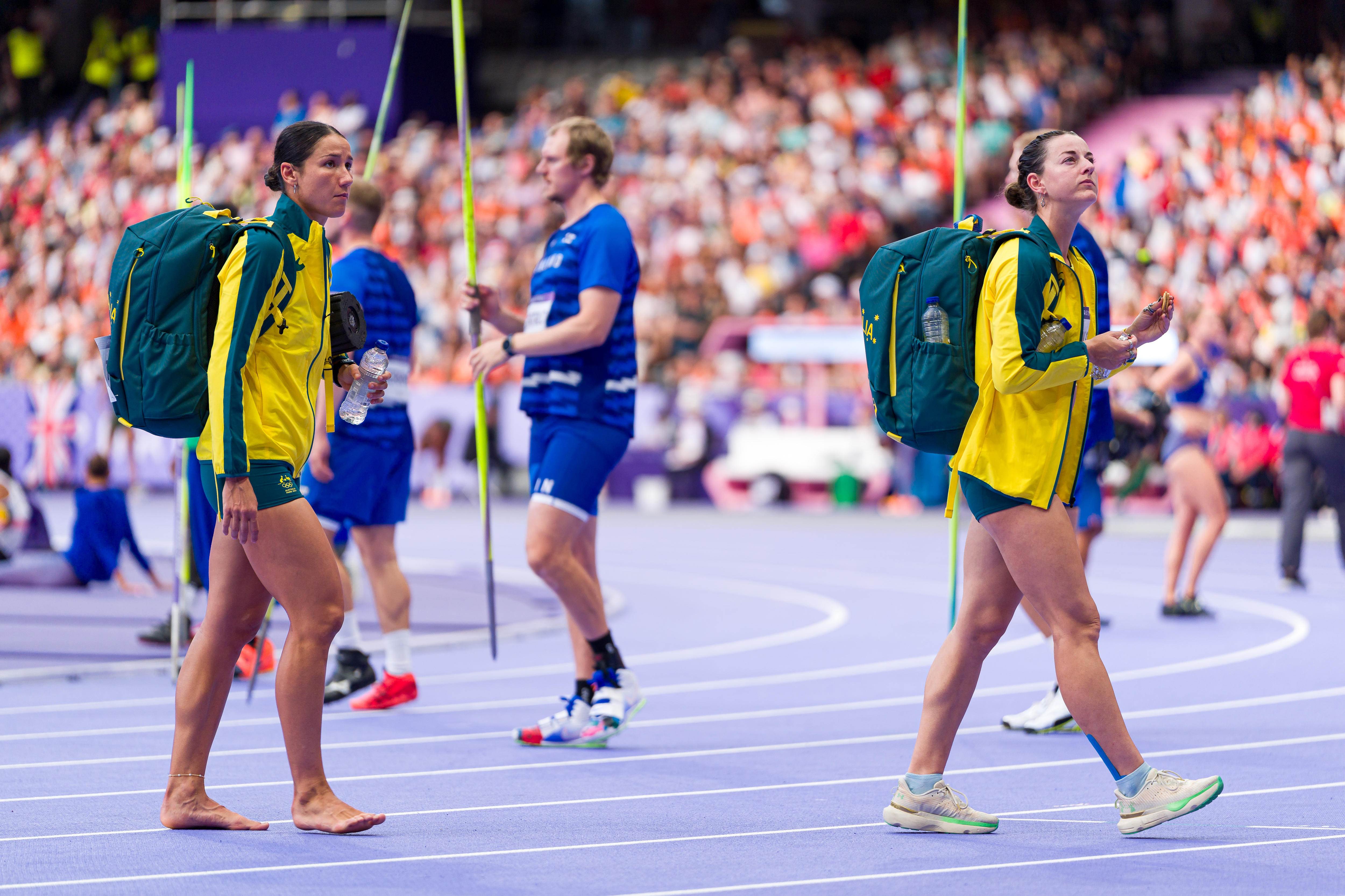 Tori West and Camryn Newton-Smith walk across the track at the Olympic Games carrying backpacks.
