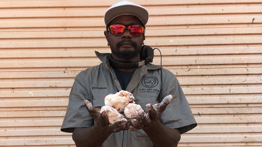 A man holds out his hands with white ochre rocks in them