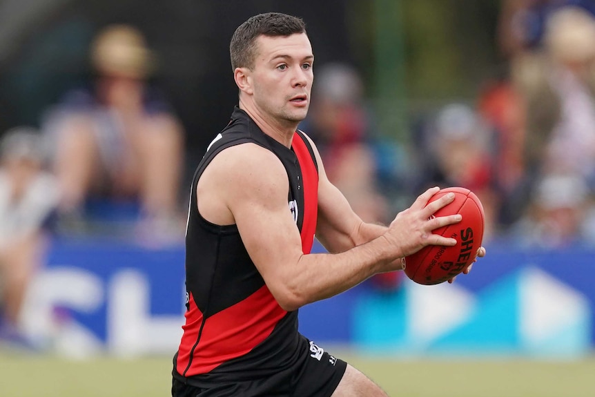 Conor McKenna holds a red AFL ball in both hands