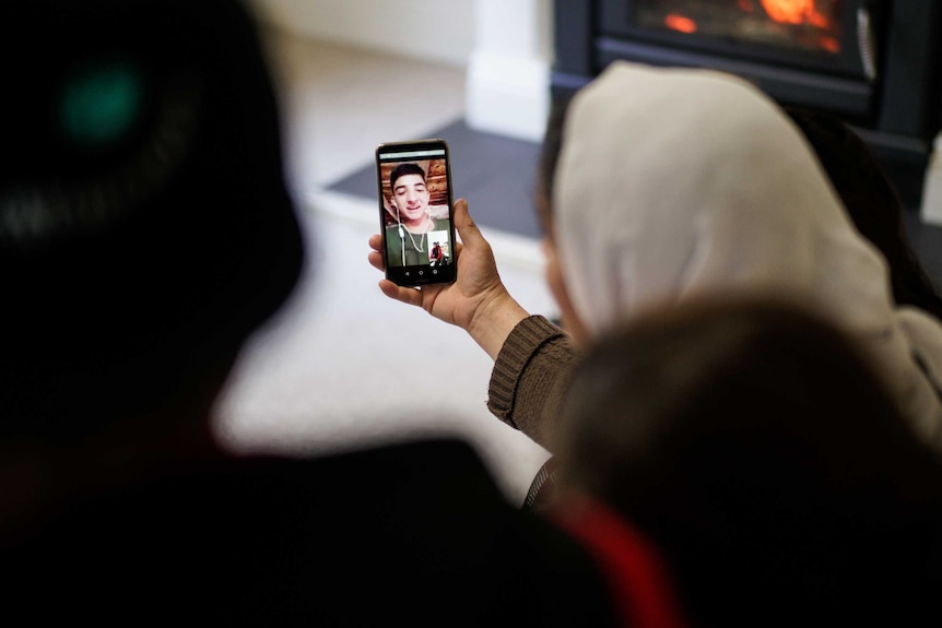 A young man appears on a mobile phone held in the hand of a woman.