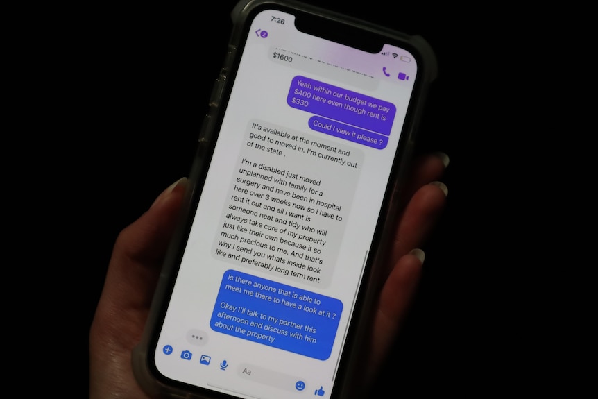 A hand holding a phone with messages from someone trying to scam them into paying for a rental that doesn't exist.