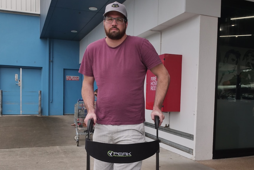 Man stands with mobility aid in a parking lot.