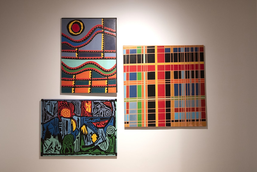 Three brightly coloured, patterned paintings hang on a wall.
