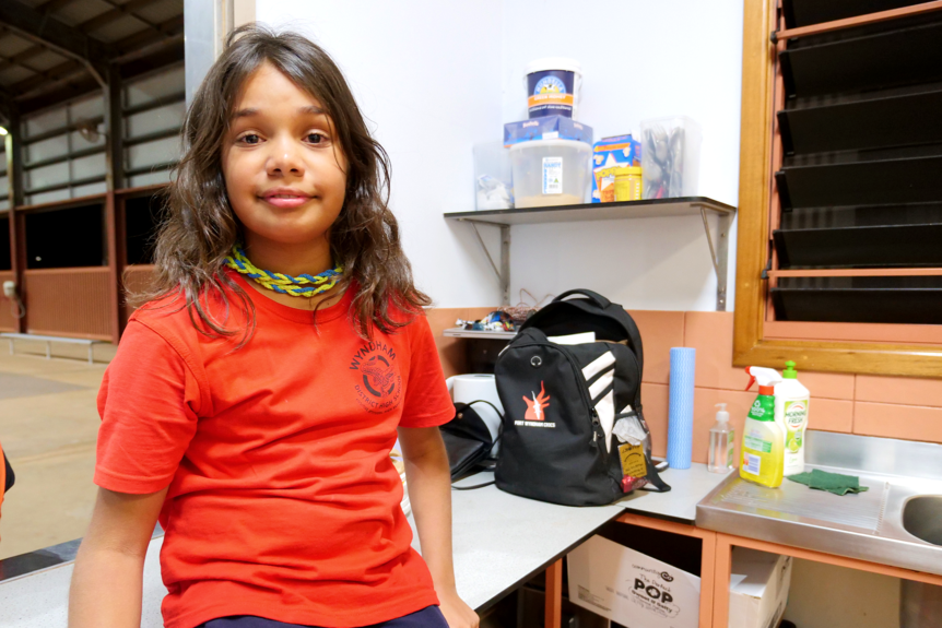 A young Indigenous girl wears her hair out to her shoulders and a bright red shirt as she sits on a counter