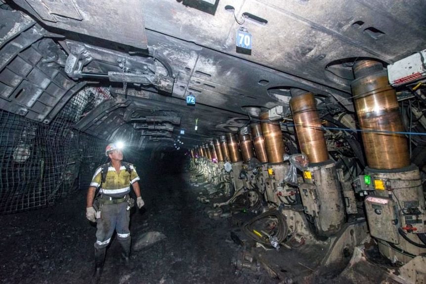 A miner in hi-vis work clothes and a hard hat inspects underground machines in a mine.