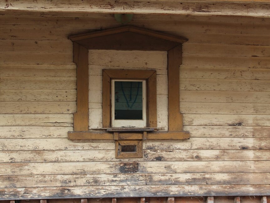 A small square window in a worn weatherboard building