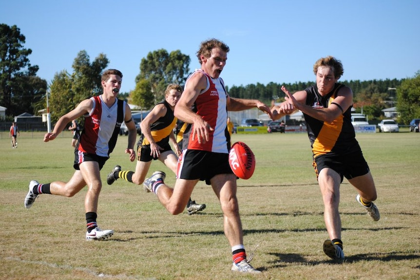 Football players on opposing teams on a field, one about to kick a ball