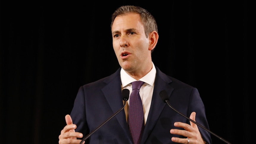 Chalmers gestures with both hands while standing in front of a lectern.