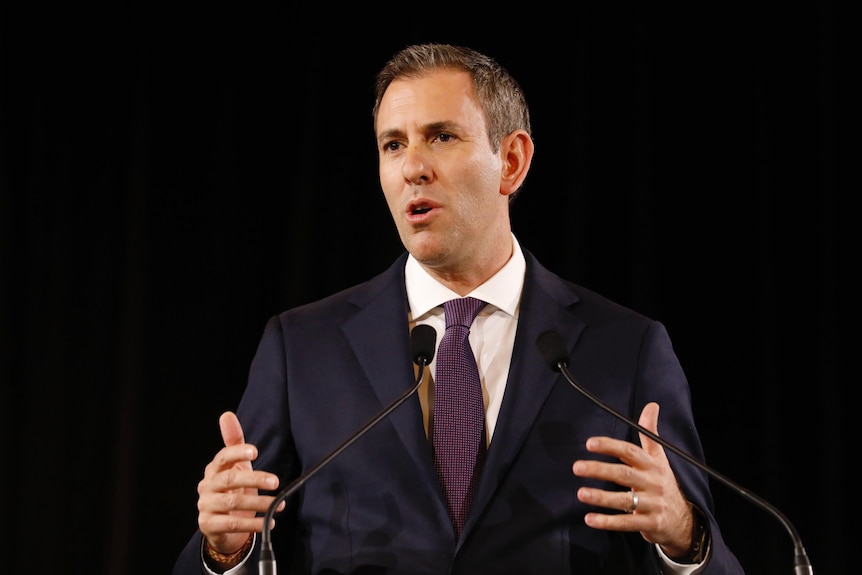 Chalmers gestures with both hands while standing in front of a lectern.