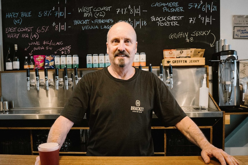 A man stands behind a bar holding a beer.