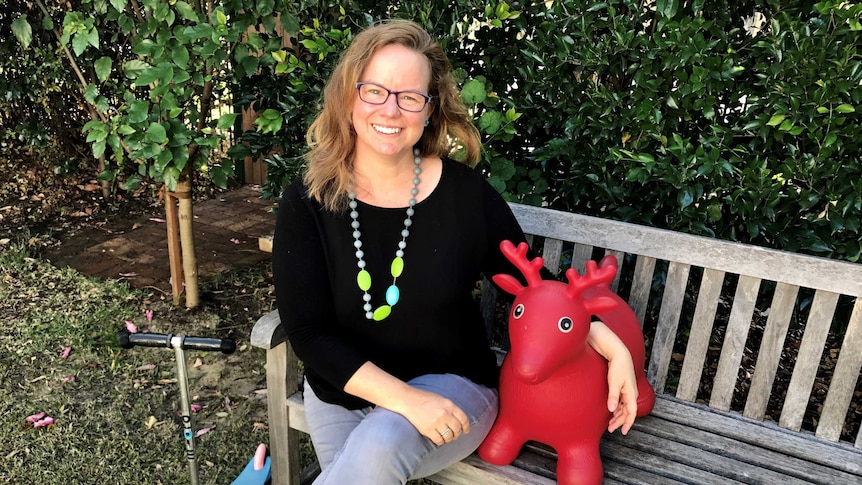 A woman sits on a garden bench with a red toy reindeer.