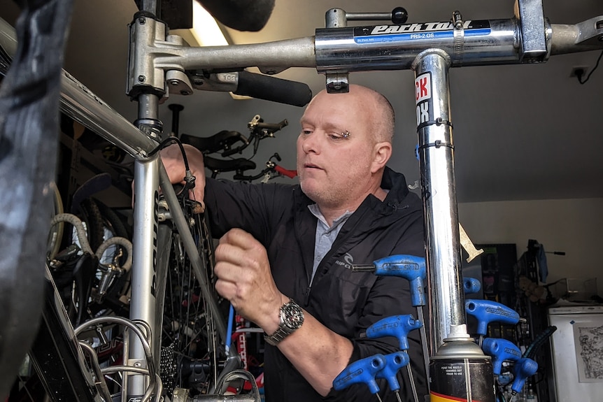 A man concentrates as he works on the frame of a bike.