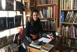 bookseller Julia Christensen sitting on a desk in a second-hand books store