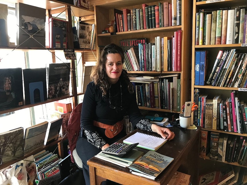 bookseller Julia Christensen sitting on a desk in a second-hand books store