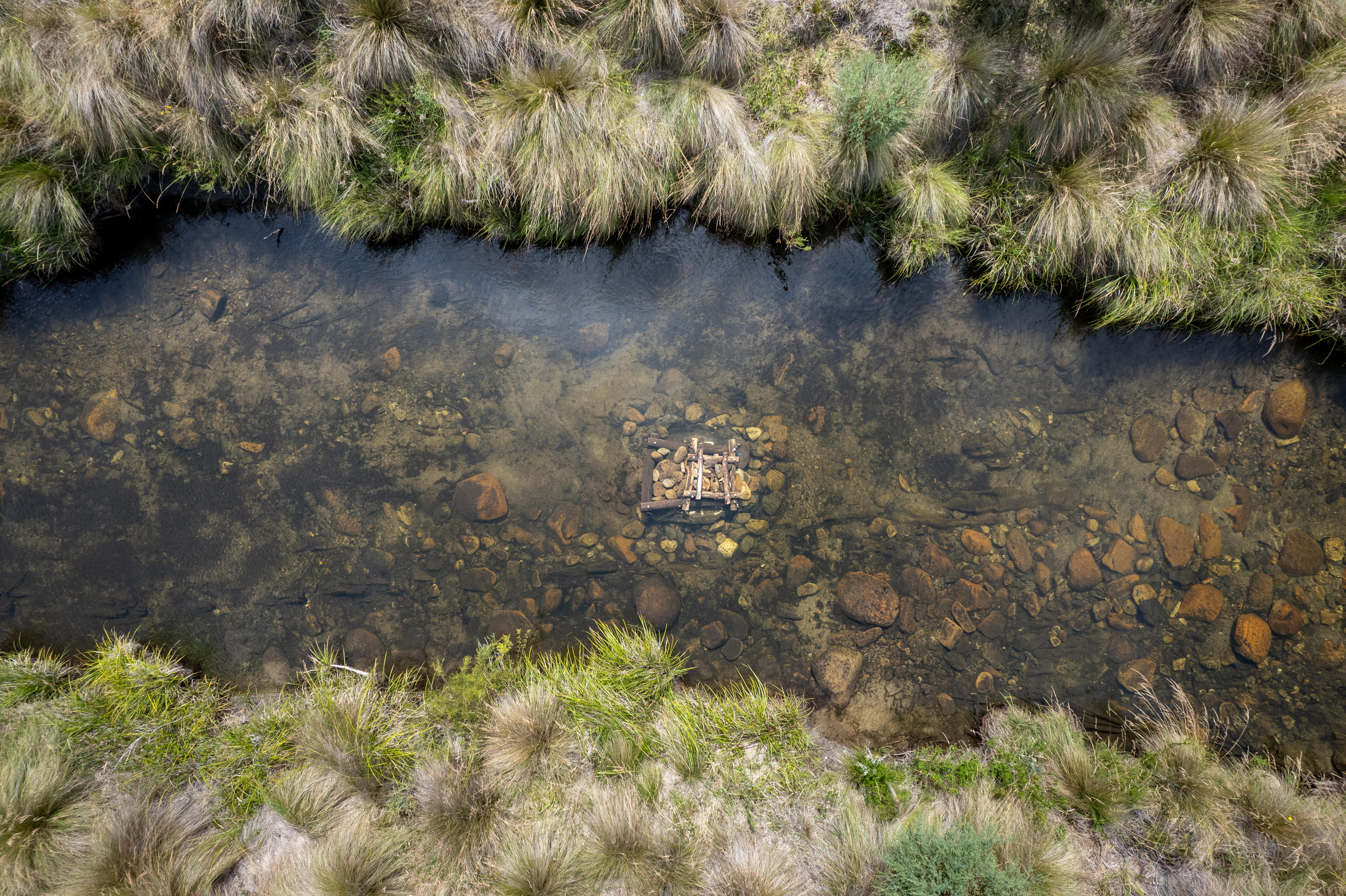 A fish hotel made of wood and rocks in the bend of a slow-moving freshwater river.