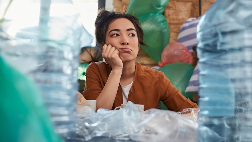 Low angle shot of an upset scruffy young woman sitting among piles of rubbish indoors