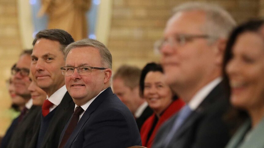 Richard Marles and Anthony Albanese sit on one side of a church aisle. Prime Minister Scott Morrison sits on the other side.