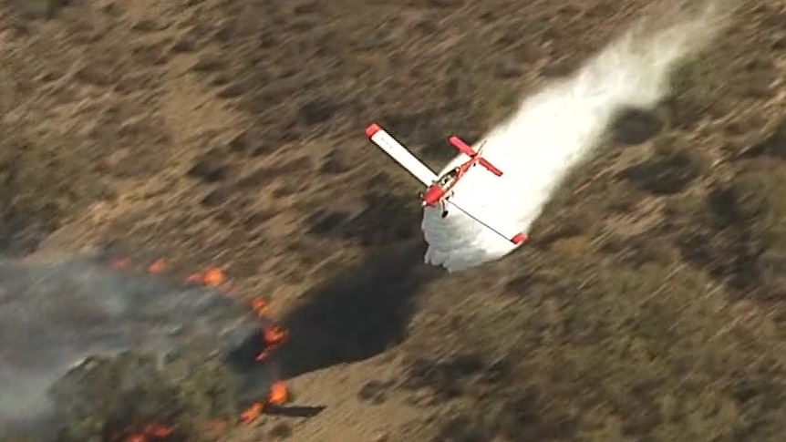 A plane dropping water on a fire and scrubland