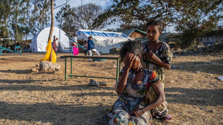 A girl braids a woman's hair at a camp for displaced persons