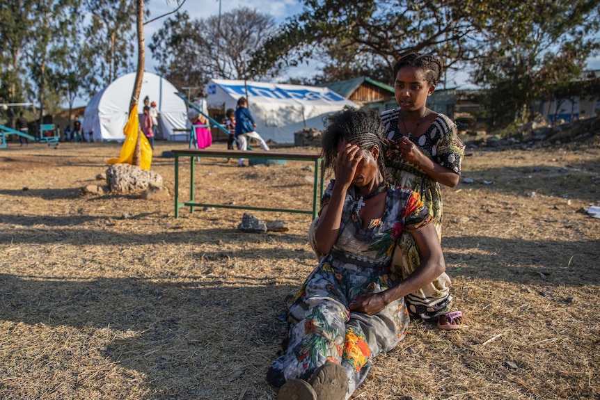 A girl braids a woman's hair at a camp for displaced persons
