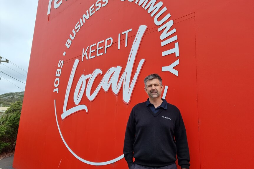 A man standing front of a sign which says "Keep It Local"