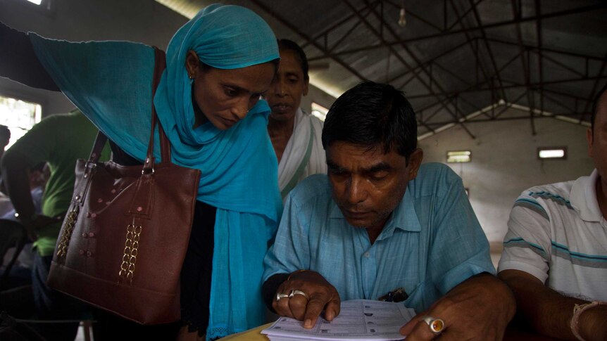 An Assam Muslim woman in a blue headscarf and a man in blue shirt check their names on the NRC list